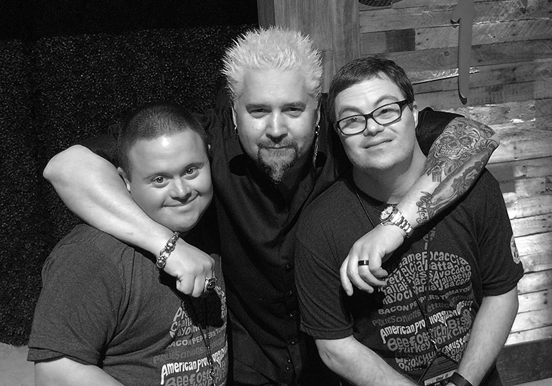 This image features Guy Fieri (middle) with Chris Gay (left) and Aaron Malman (right). The three are posing together, smiling, and appear to be in a friendly and supportive setting.