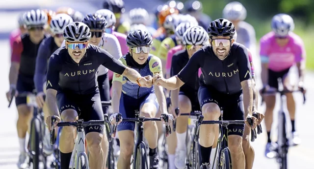 Cyclists participating in the 25th Anniversary Best Buddies Challenge: Hyannis Port, with two riders from Team Aurum fist bumping in the foreground.