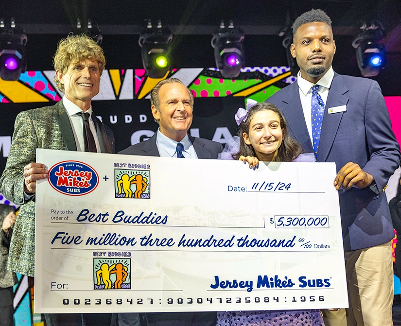 Anthony K. Shriver, Jersey Mike’s Subs Founder Peter Cancro, and two Best Buddies Ambassadors, are holding a giant ceremonial check for $5,300,000 at the Jersey Mike's Subs Best Buddies Miami Gala on November 15, 2024.