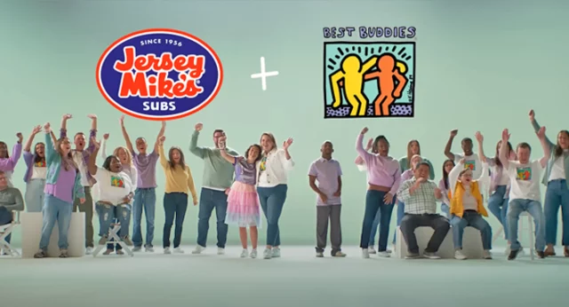 The image shows a group of diverse individuals, some of whom are raising their arms in celebration, standing together beneath the logos of Jersey Mike's Subs and Best Buddies International. The Jersey Mike's Subs logo is on the left, while the Best Buddies logo, featuring two figures outlined in yellow and orange, is on the right.