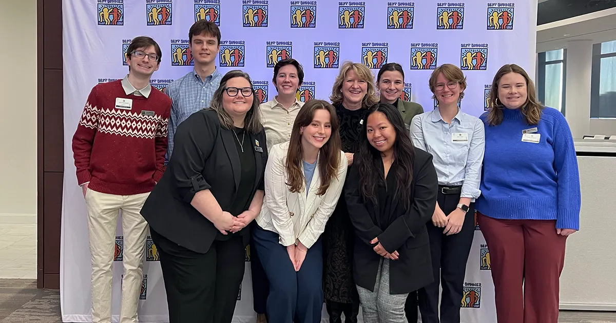 10 best Buddies in Virginia & DC staff members posing for a group photo in front of a set and repeat with the blue, yellow, and orange Keith Haring Best Buddies logo.