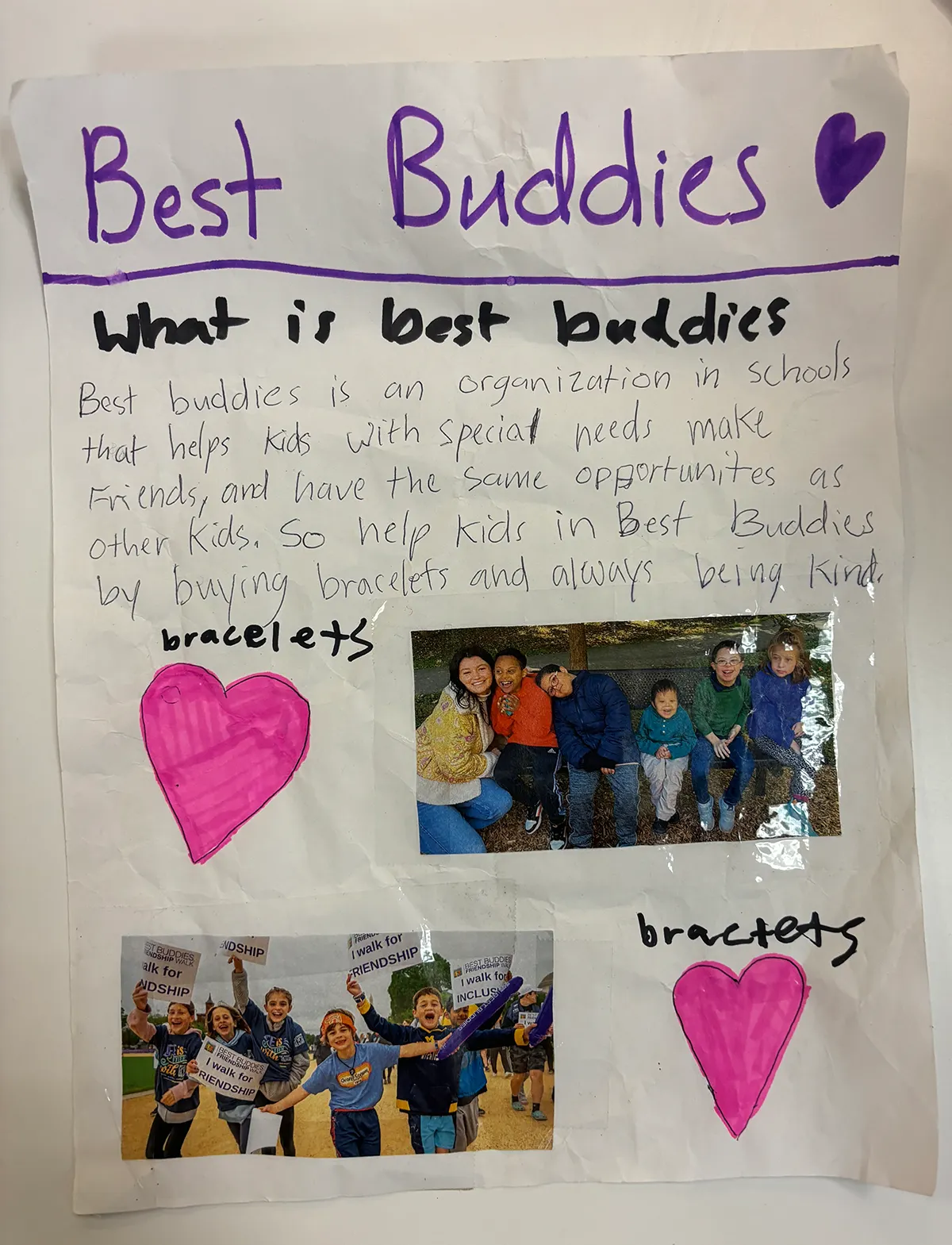 A hand-written flyer advertising the friendship bracelet sale. “Best Buddies” is written at the top in purple marker with a purple heart. There are two pink hearts and two photos of elementary school children with and without intellectual and developmental disabilities smiling and having fun together.