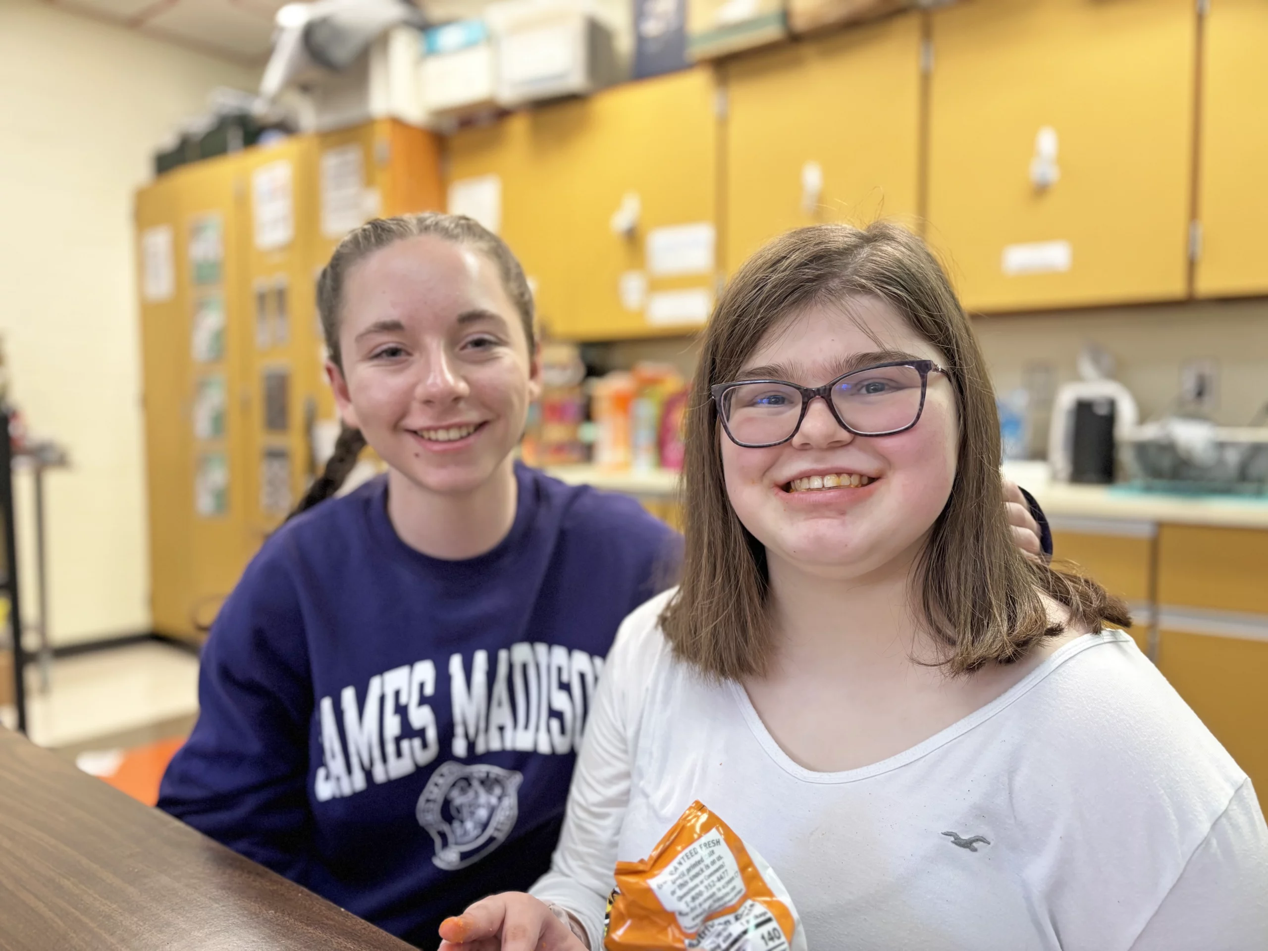 Two friends smiling together in a classroom.