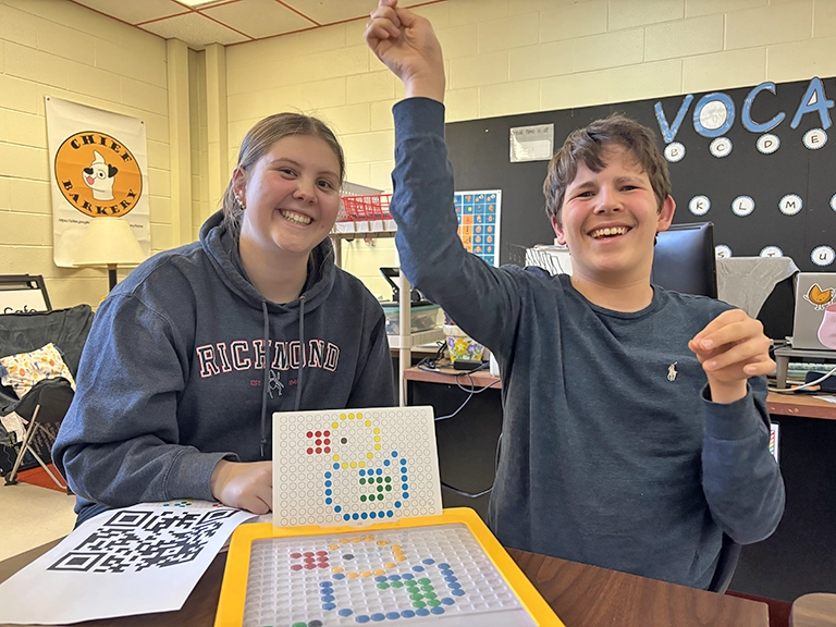 Two friends smiling and playing board games together in a classroom.